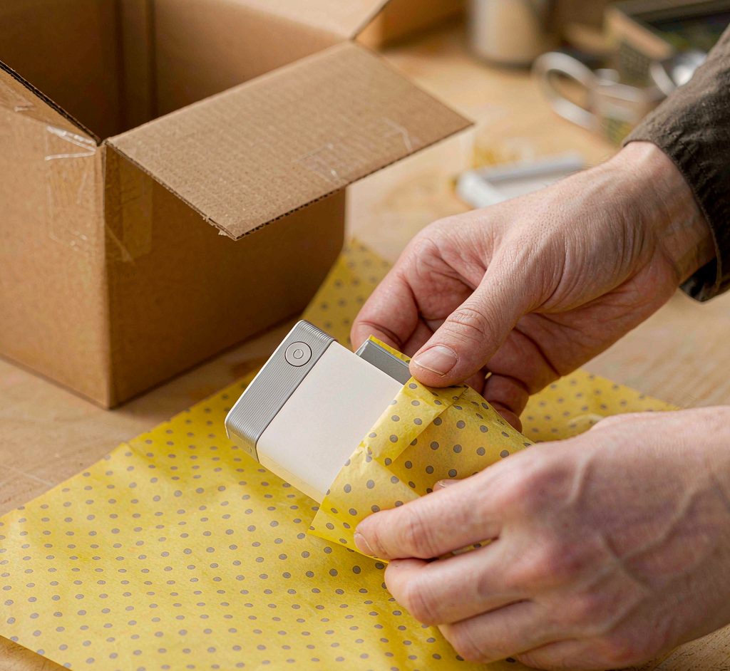Hands wrapping a product in tissue paper before boxing at a fulfillment workbench